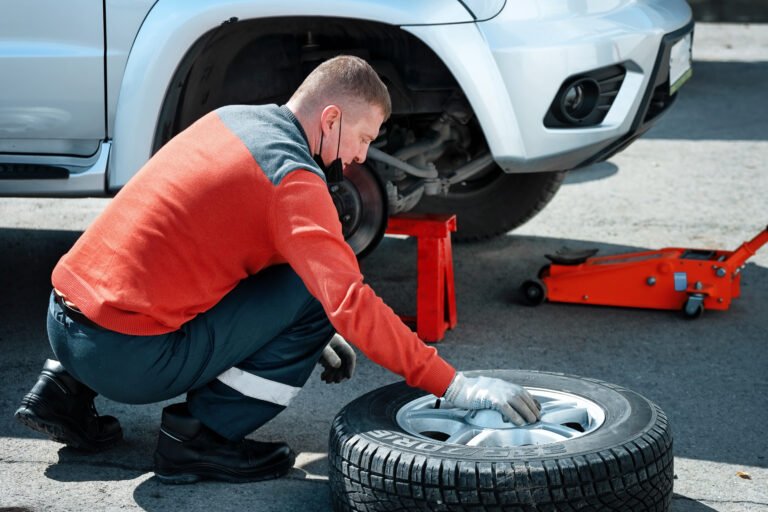 A car mechanic in a medical mask changes a wheel on a car on the street on a sunny day